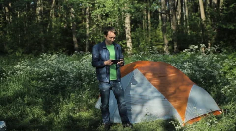 A man playing on a tablet next to the tent in the forest, early morning Stock Footage 64328340