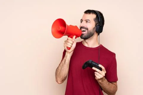 Man playing with a video game controller over isolated wall shouting through  Stock Photos