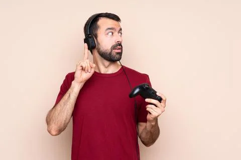 Man playing with a video game controller over isolated wall thinking an idea  Stock Photos