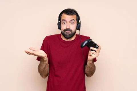 Man playing with a video game controller over isolated wall having doubts whi Stock Photos