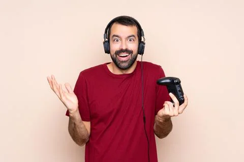 Man playing with a video game controller over isolated wall with shocked faci Stock Photos