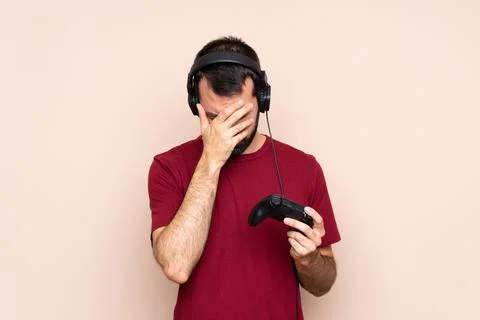 Man playing with a video game controller over isolated wall with tired and si Stock Photos