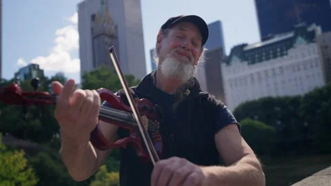Man playing Violin in Central Park On Bridge NYC New York Manhattan Buildings Vídeo Stock 240240347