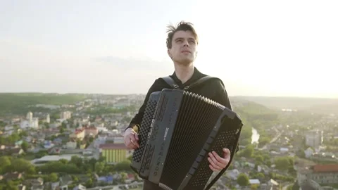 A man plays the accordion at sunset with a view of the city. Smooth moving Stock Footage 242427985