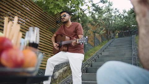Man plays an acoustic guitar while others relax and enjoy the warm weather Video stock 278816560