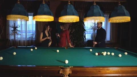 A man plays Billiards and two young beautiful women watching the game Stock Footage 70398692
