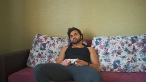 A man plays the console while lying on the couch during self-isolation. Stock Footage 127710841