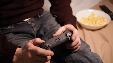 A man plays a game console with a joystick. Popcorn, TV remote Stock Footage 146450037