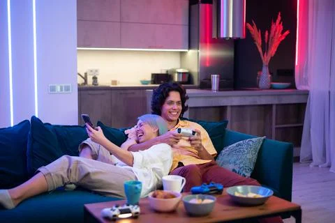 Man plays on gaming console using joystick while woman using smart phone with Stock Photos
