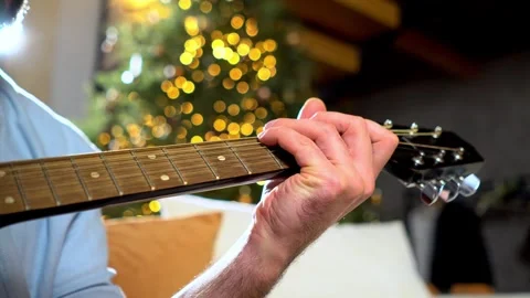 Man plays guitar and changes chords against the background of Christmas tree Stock Footage 294324885