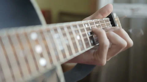 A man plays the guitar close up while sitting at a window in the apartment Stockbeeldmateriaal 64899420