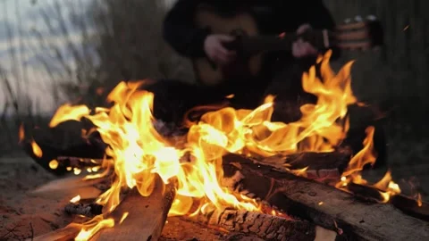 A man plays the guitar. In the foreground is a fire. Summer evening. Slow motion Stock Footage 130730337