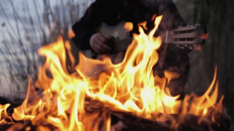 A man plays the guitar. In the foreground is a fire. Summer evening. Slow motion Video stock 130730734