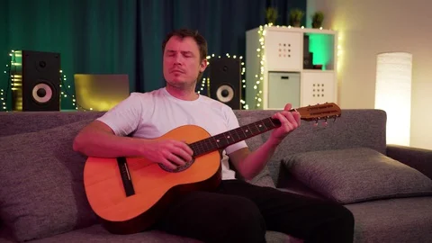A man plays guitar sitting on the couch Stock Footage 129101360