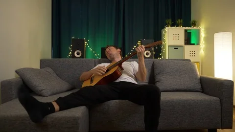 A man plays guitar sitting on the couch Stock Footage 129384363