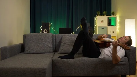 A man plays a guitar while lying on the couch Stock Footage 129384460