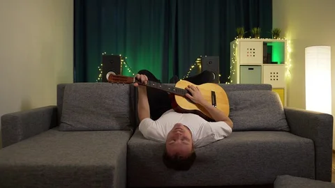 A man plays a guitar while lying on the couch Stock Footage 129384467