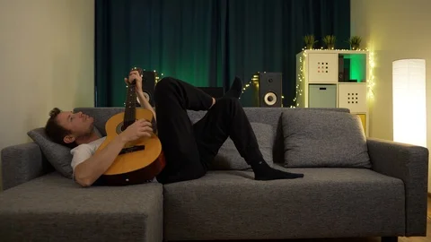 A man plays a guitar while lying on the couch Stock Footage 129384491