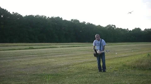 MAN PLAYS GUITAR WHILE PLANE FLIES OVER HIS HEAD Stock Footage 12110881
