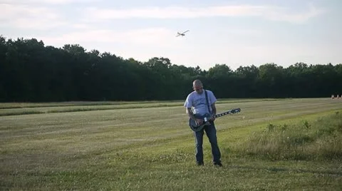 MAN PLAYS GUITAR WHILE PLANE FLIES OVER HIS HEAD Stock Footage 12110956