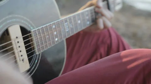 A man plays the guitar while sitting by the sea. Close up Stockbeeldmateriaal 64901195