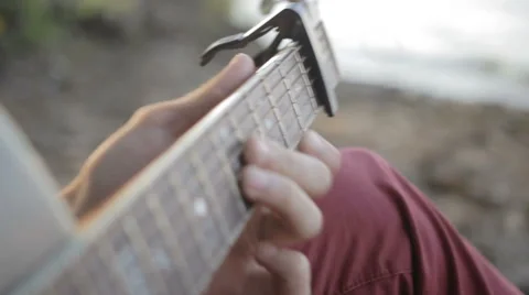 A man plays the guitar while sitting by the sea. Close up Vídeo Stock 64901695
