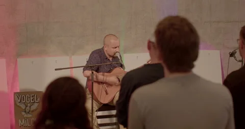 Man plays guitar while sitting on a chair. He makes tune for audience. Stock Footage 200778661