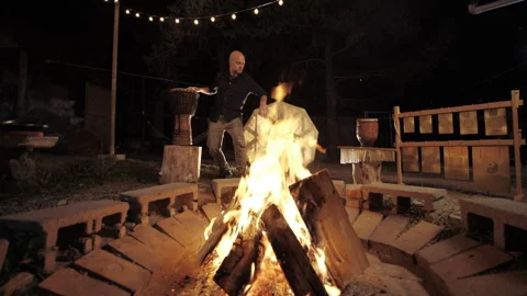 A man plays hand jemba drums by a fire at night, embracing nature's rhythm. Video stock 300890293