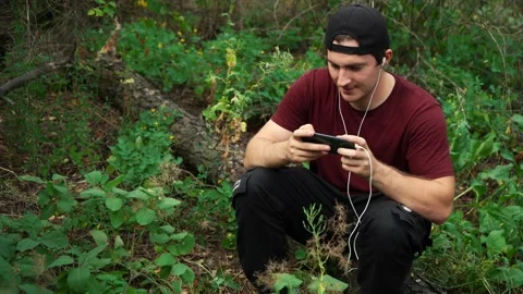 Man plays on the phone while sitting in the forest on a fallen tree. being in Stock Footage 158815847