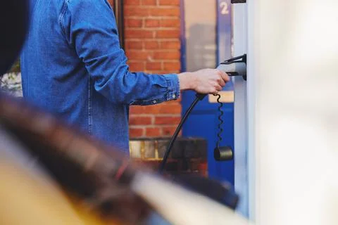 Man plugging in electric car to charging point outside home Stock Photos