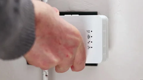 Man plugging a typical NETGEAR WiFi extender into a home wall outlet. With s Stock Footage 171007088