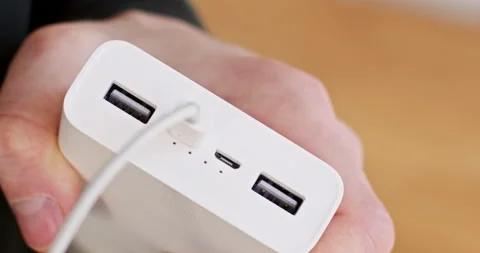 Man plugs micro USB cord to powerbank on blurred background 動画素材 235897377