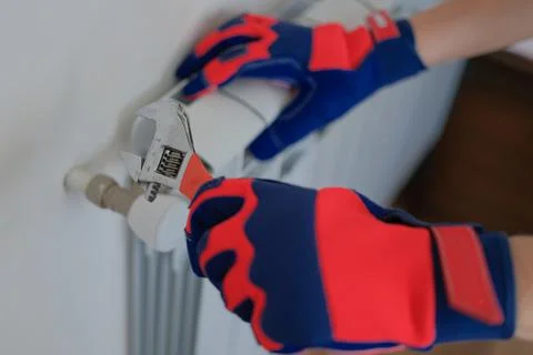 Man plumber hands in gloves installing heating radiator using wrench Stock Photos
