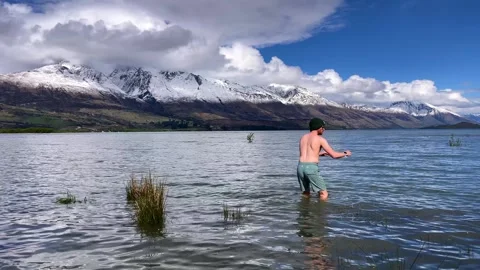 Man plunges into cold waters of Lake Wakatipu near the snow-capped peaks of New Video stock 302552736