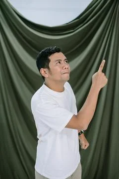 Man pointing up with curious expression against a draped backdrop Foto stock