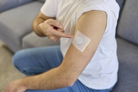 Man pointing at glucose sensor patch on upper arm, wearable diabetes device 스톡 사진