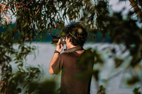 Man pointing his camera with hand held near the lake. Man taking photo with.. Stock Photos