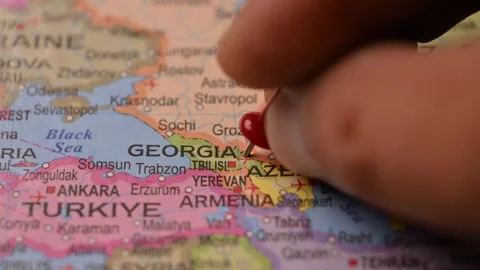 Man Pointing Red Pin on Georgia Location on Paper World Map Close Up Stock Footage 333551792