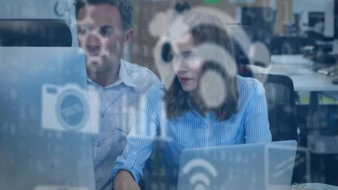 Man pointing at screen while woman typing laptop, initiating tech icons on glass Stock Footage 334040824