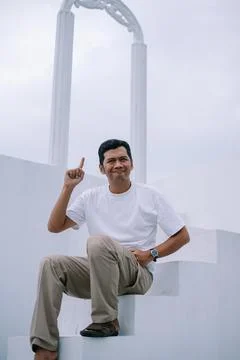 Man Pointing Upward While Sitting on Steps with White Archway Behind Stock Photos