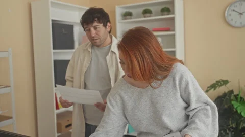 Man points to computer monitor while holding printed papers as woman reads .. Stock Footage 337391764