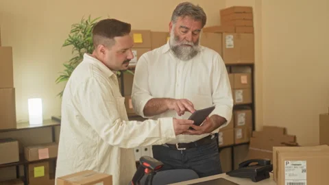 Man points finger at tablet while another worker holds it amid stacked card.. Video stock 339214376