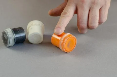 A man points to orange paint in a container with his index finger. Three cyli Stock Photos