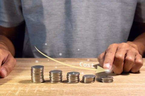 A man points at a stack of coins with a down arrow. Cost reduction concept. Stock Photos