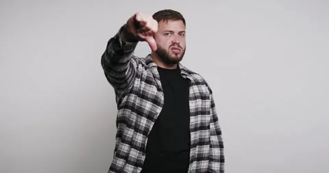 Man points thumbs down while standing in a studio with a plain background Stock-Footage 326798026