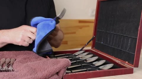 Man polishing a fork with cloth, cleaning cutlery set in wooden box, househol Stock Footage 315212134