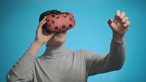 Man in polo neck with VR headset catches something on blue Stockbeeldmateriaal 130430456