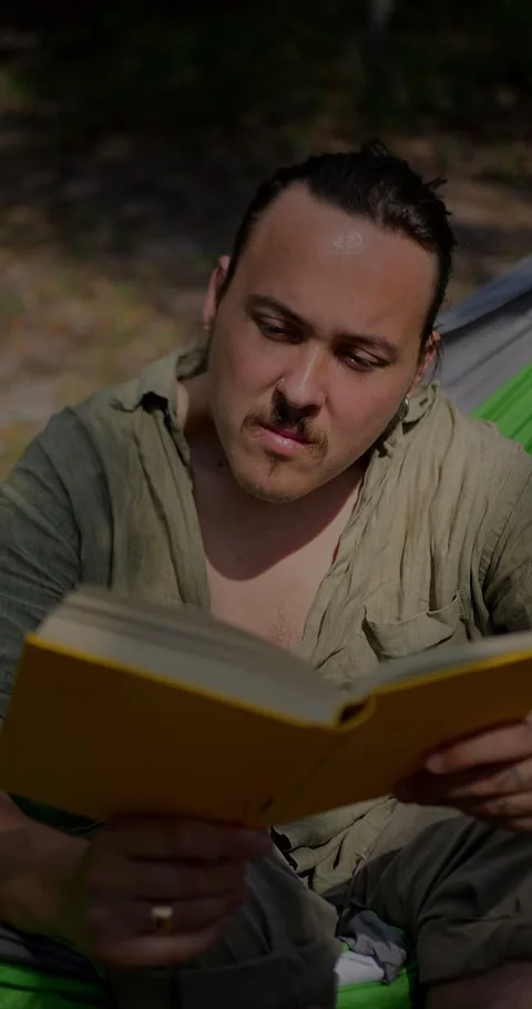 Man With Ponytail And Mustache Reading Yellow Book... Stock Footage 331820863