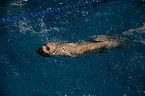 Man in the pool. Floating on his back. A swimmer trains in the pool on the track Stock Photos