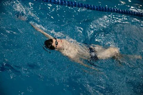 Man in the pool. Floating on his back. A swimmer trains in the pool on the track Stock Photos